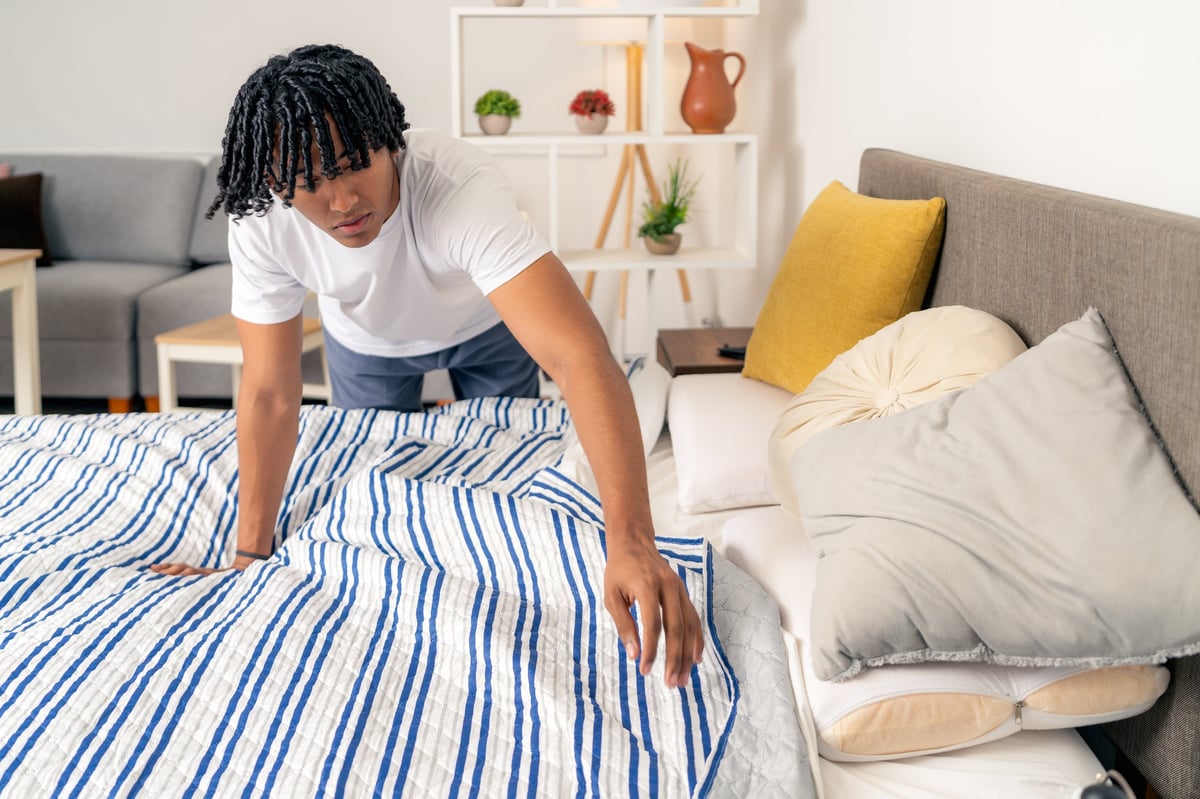 Young man tidying his bedroom, arranging sheets and pillows